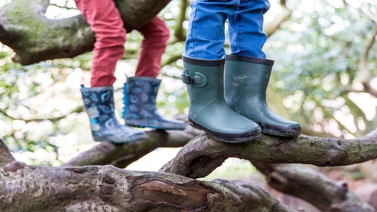 Picture shows children in wellies climbing a tree.